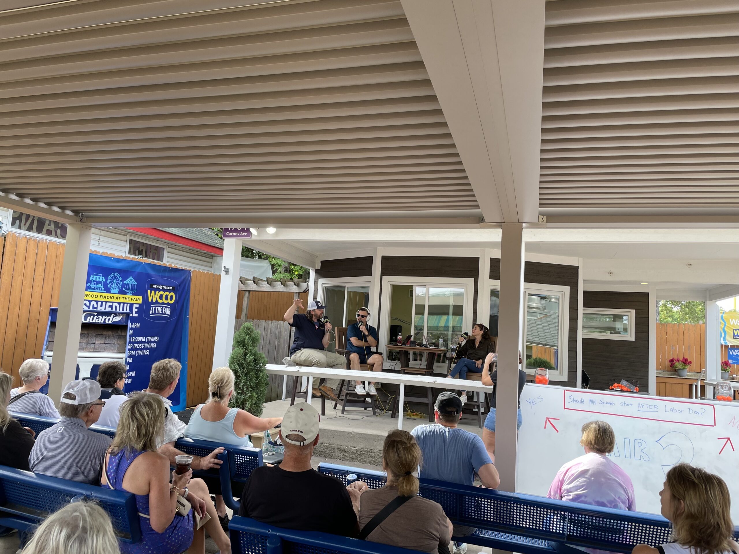 Fairgoers seated beneath the StruXure Pergola X while watching a live WCCO Radio broadcast at the Minnesota State Fair.